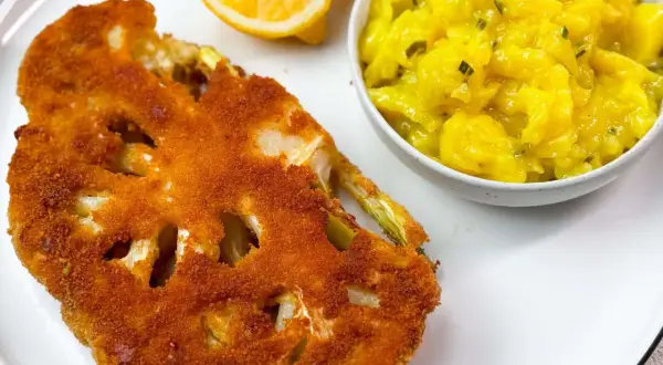 Knuspriges Blumenkohl-Schnitzel mit Kartoffelsalat und Zitronenspalten auf einem weißen Teller.