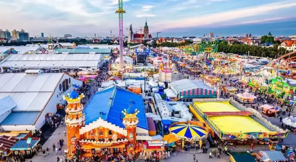Aerial view of a crowded Oktoberfest fairground with tents, rides, and people.