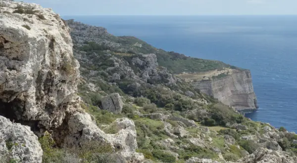 Malta's dramatic Dingli Cliffs, a rugged coastline meeting the deep blue sea under a cloudy sky.