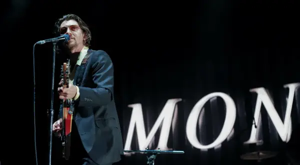 Alex Turner w okularach przeciwsłonecznych śpiewa i gra na gitarze podczas jednego z koncertów Arctic Monkeys.