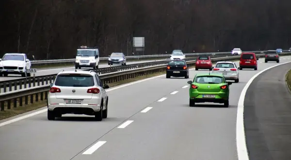 Zielony Seat wyprzedza białe auto, ryzykując wymuszenie pierwszeństwa na autostradzie. W tle inne pojazdy.