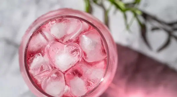 En rosa drink med hjärtformade isbitar och en rosmarinkvist.