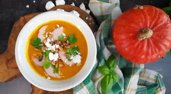 Pomarańczowa zupa dyniowa z mięsem, serem feta, orzeszkami i kolendrą, obok dynia.