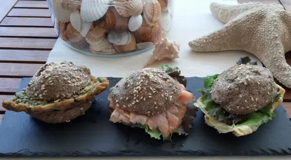 Tre panini low carb ricetta: uno con pesto, uno con salmone affumicato e insalata, uno con formaggio e insalata. Decorazioni marine sullo sfondo.