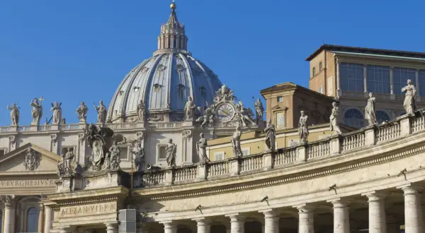 Cupola maestosa e colonnato di San Pietro, una delle quattro basiliche di Roma, con statue che vegliano sul cielo azzurro.