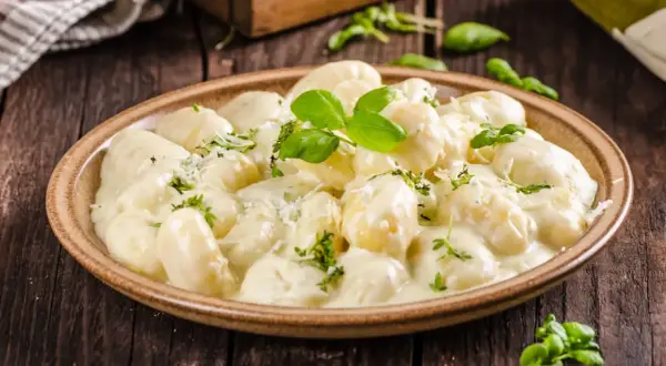 Pyszne gnocchi z kurczakiem w kremowym sosie, posypane parmezanem i świeżą bazylią. Idealne danie na obiad.