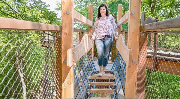Frau genießt den Ausblick auf dem baumwipfelpfad Usedom. Holzkonstruktion mit Netzen und Seilen führt durch grüne Baumkronen.