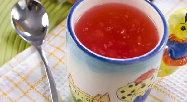 Czerwony kisiel w kubeczku z bajkowym wzorem, obok łyżeczka. Idealny deser, gdy liczymy kisiel kcal.