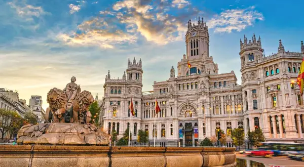 Cibelesfontänen framför det ståtliga Palacio de Comunicaciones, ett ikoniskt konstmuseum i Madrid, under en dramatisk solnedgång.