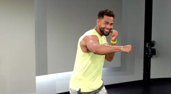 A smiling man in a yellow tank top throws a side hook punch, ready for his next workout move.