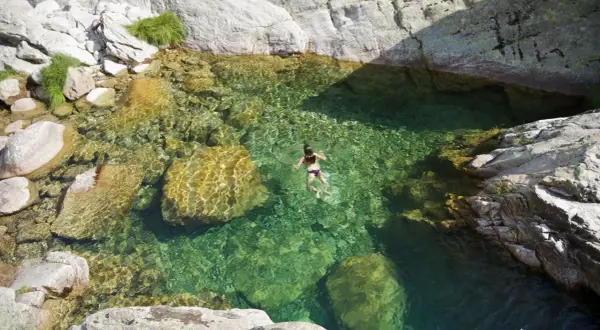 Una persona nada en pozas naturales de agua cristalina en la sierra de Madrid, rodeada de rocas y vegetación.