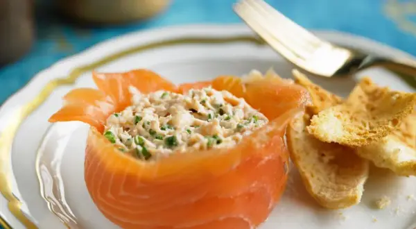 Ein appetitlicher **Salat mit Fisch**, serviert in einem Lachs-Cup, mit knusprigen Brotscheiben und einer goldenen Gabel.