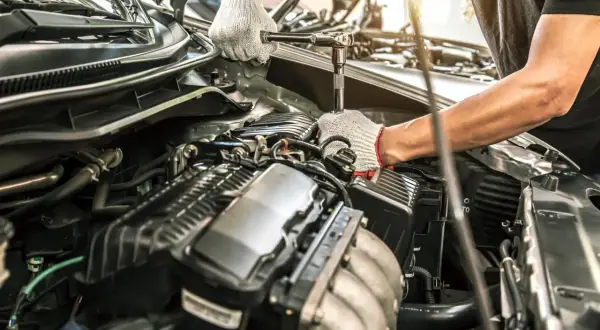 Mechanik w białych rękawiczkach dokręca śrubę w silniku benzynowym. Może to być przyczyną falujących obrotów na ciepłym silniku.