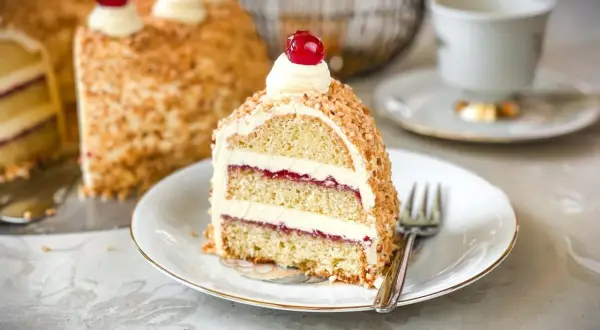 Ein Stück Frankfurter Kranz mit Buttercreme und Kirschen, umhüllt von gehackten Nüssen. Ein Genuss für jeden Kaffeetisch.