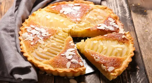 Une délicieuse tarte aux poires, garnie d'amandes effilées et saupoudrée de sucre glace, repose sur une table en bois.