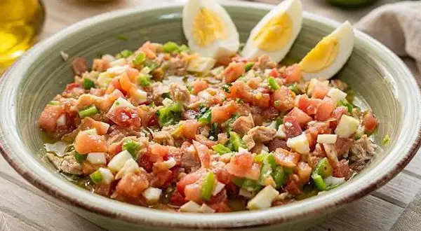 Un refrescante plato de pipirrana andaluza, con tomate, pimiento, huevo duro y atún, listo para disfrutar.