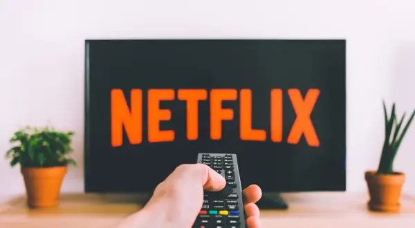 En hand håller en fjärrkontroll framför en TV med Netflix-loggan. Perfekt för bra filmtips ikväll!