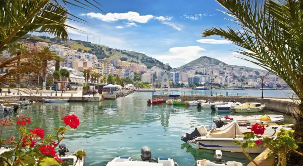 Albania - wczasy samolotem all inclusive. Widok na port z łodziami i kolorowymi budynkami na wzgórzu.