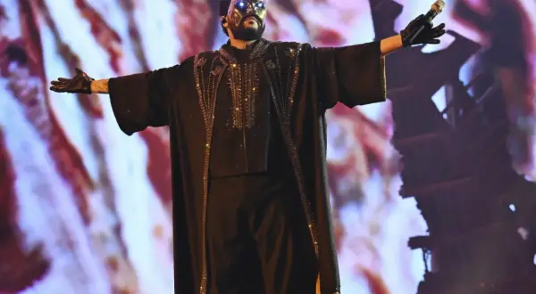 The Weeknd w masce i błyszczącym stroju na koncercie w Polsce, z rękami rozłożonymi szeroko.