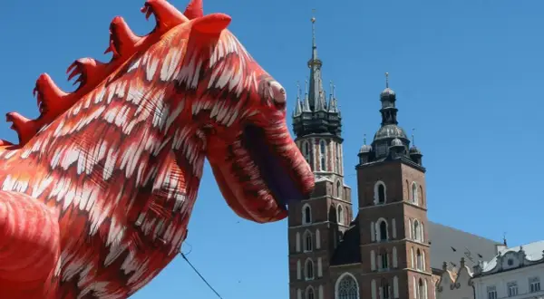 Smok wawelski, znany z atlas obscura krakow, wita turystów na tle Kościoła Mariackiego.
