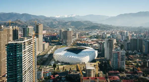 Widok na nowoczesne miasto z futurystycznym stadionem i górami w tle. Rozwój infrastruktury, budowa nowych wieżowców. Batumi ceny nieruchomości mogą być tu atrakcyjne.