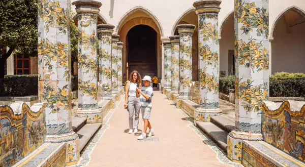 Cortile con colonne decorate a maiolica, un classico del museo Napoli. Una madre e un figlio passeggiano tra gli archi.