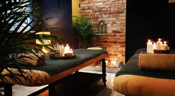 Dwie łóżka do masażu w przytulnym spa, ozdobione świecami i roślinnością.