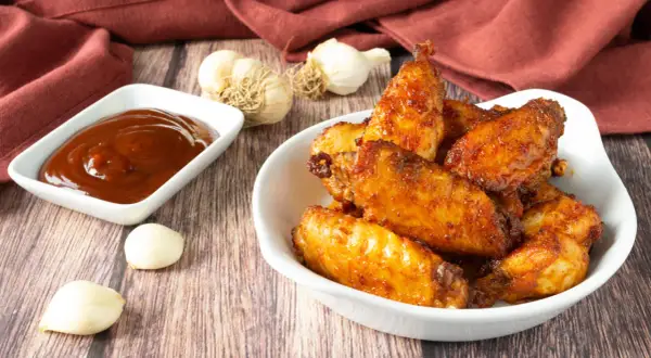 Alette di pollo croccanti e dorate, appena sfornate dalla friggitrice ad aria, servite con salsa barbecue e aglio.