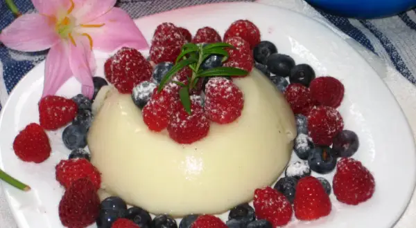 Panna cotta z malinami i borówkami, posypana cukrem pudrem. Idealny deser, który można przygotować według prostego legumina przepisu.
