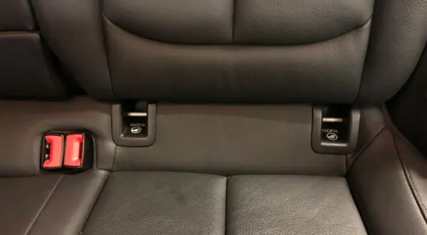 Widok na tylne siedzenia samochodu z widocznymi zaczepami **isofix jak wygląda** oraz czerwonymi klamrami pasów bezpieczeństwa.