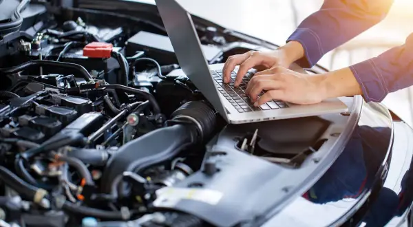 Mechanik diagnozuje brak mocy na ciepłym silniku benzyna, używając laptopa do analizy danych z jednostki napędowej.