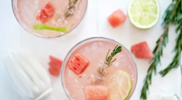 Två glas med en rosa, alkoholfri drink med is, vattenmelonbitar, lime och rosmarin. Perfekt för en sommardag.
