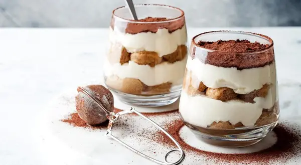 Dwa pucharki z kremowym tiramisu, posypane kakao. Idealna mizeria na słodko, która rozpływa się w ustach.