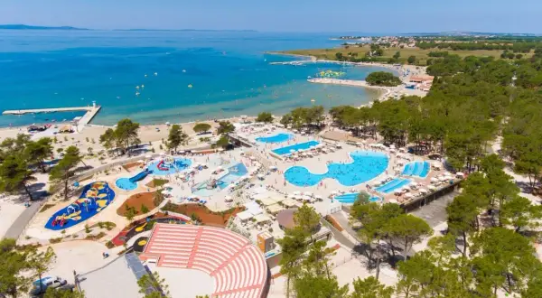Widok z lotu ptaka na kompleks basenów i plażę z turystami w słoneczny dzień.