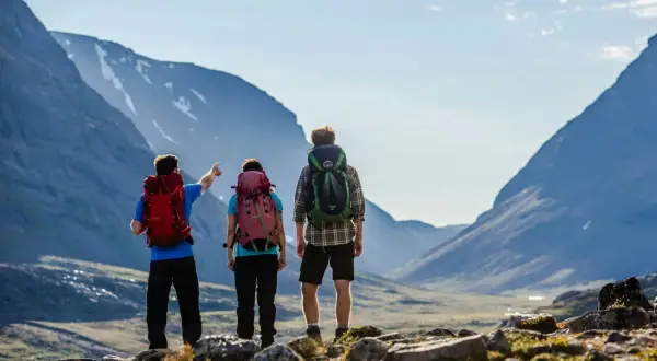 Två vandrare med ryggsäckar blickar ut över en dalgång i Abisko. En pekar mot bergen.