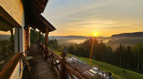 Wschód słońca nad Bieszczadami, widok z tarasu drewnianego domu. Mgła spowija doliny, tworząc malowniczy krajobraz.