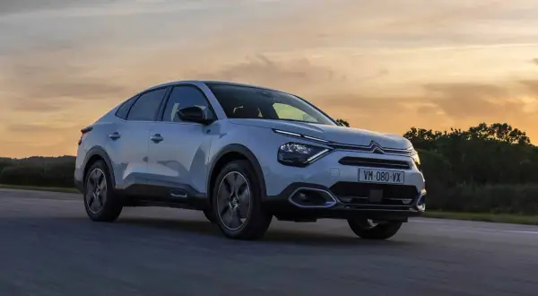 Jasnoszary Citroën C4X sunie po drodze podczas zachodu słońca.