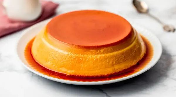 Delizioso creme caramel su un piatto bianco, con sciroppo ambrato che cola sui lati.