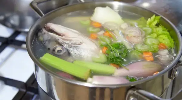 Une tête de poisson nage dans un bouillon avec des légumes, promettant un fumet de poisson savoureux.