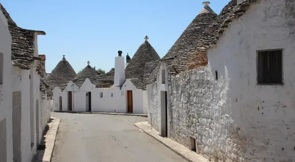 Strada tra i trulli, un incantevole esempio dei borghi da visitare in Puglia. Case bianche con tetti conici in pietra sotto un cielo azzurro.