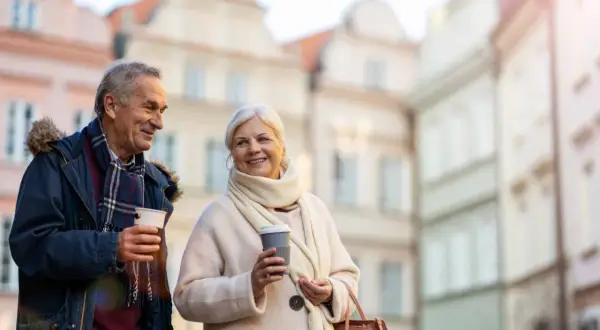 Uśmiechnięta para seniorów z kawą na spacerze. Idealne wycieczki dla seniorów samolotem, by odkrywać nowe miejsca.