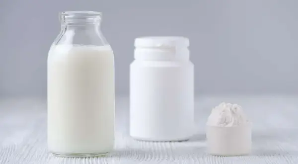 Bottiglia di latte, contenitore bianco e misurino con polvere. Le proteine del latte si trovano in questi prodotti.
