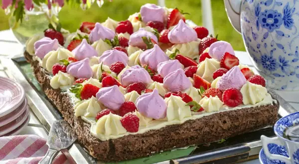 En chokladkaka i långpanna, dekorerad med grädde, maränger och färska bär. Perfekt för ett sommarfika.