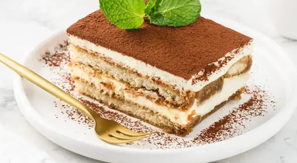 Pyszny kawałek tiramisu z mascarpone, posypany kakao i udekorowany miętą. Idealny na deser.