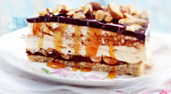 Ein Stück cremiger Käsekuchen mit Schokoladenglasur, Karamell und Nüssen als köstliches cheesecake topping.