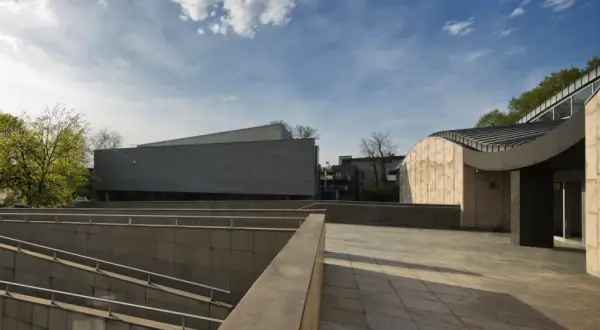 Nowoczesna architektura muzeum sztuki i techniki japońskiej Manggha z kamiennymi fasadami i zielenią w tle.