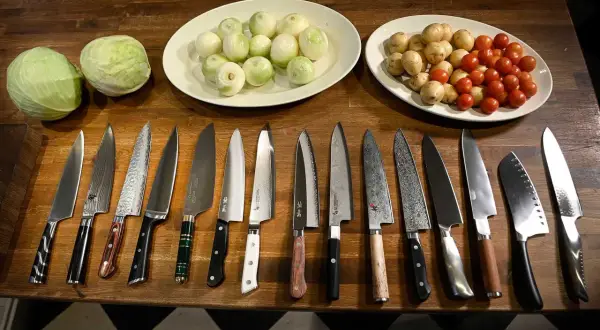 En samling vassa köksknivar ligger uppradade på en träbänk, redo att ta sig an kål, lök och tomater. Varje bra kökskniv är ett verktyg för kulinariska äventyr.
