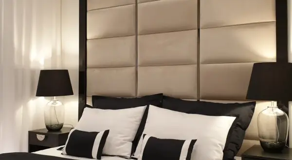 Elegancka sypialnia w stylu hotelowym. Miękkie, pikowane wezgłowie, czarno-biała pościel i stylowe lampki nocne tworzą luksusową atmosferę.