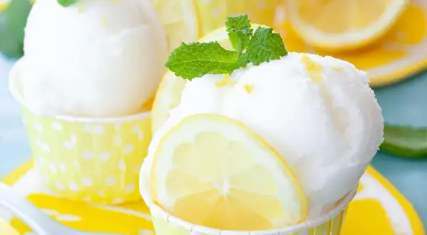 Erfrischendes Zitronensorbet-Rezept: Kugeln in gelben Tupfenförmchen, garniert mit Zitronenscheiben und Minze.