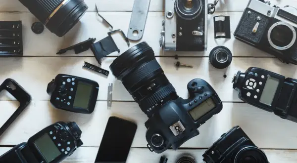Rozłożone na białym tle aparaty fotograficzne, obiektywy i lampy błyskowe.